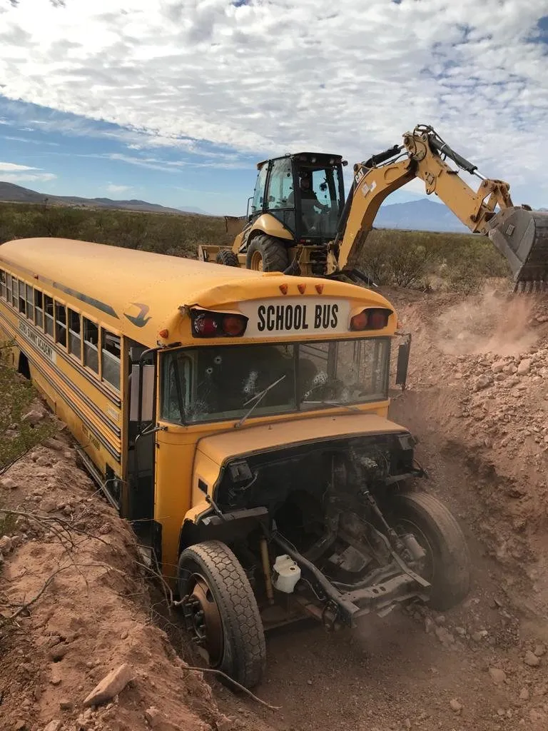 A yellow school bus nose-down in a freshly dug pit as an excavator works behind it