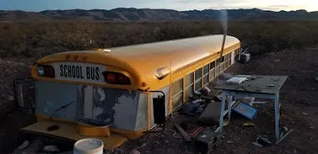 The buried school bus at dusk, with a work table set up beside it