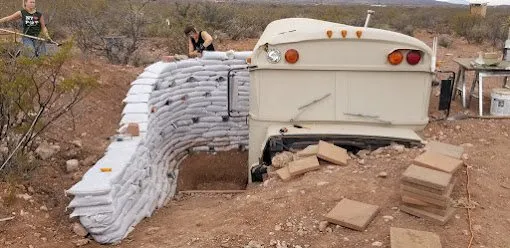 Earthbag walls built up around the end of the buried bus