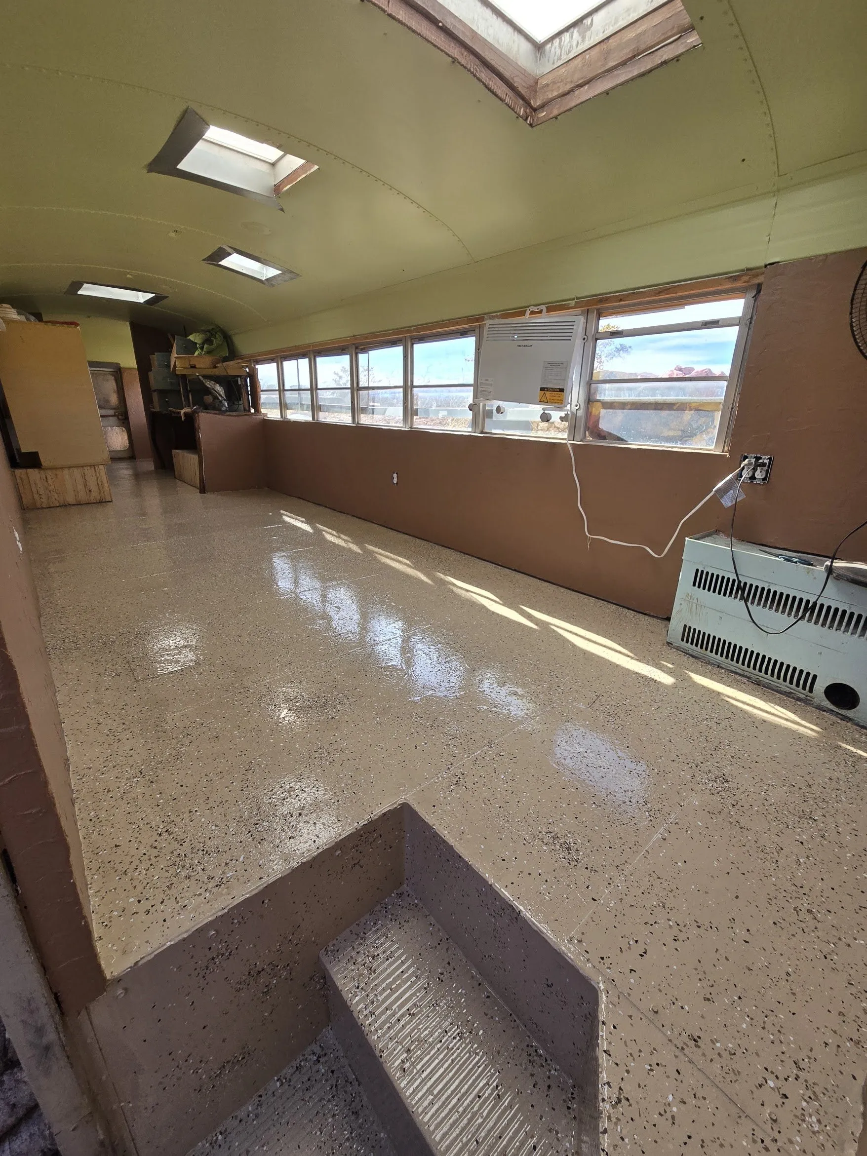 Inside the bus during renovation: a long open room with a skylight and tiled floor