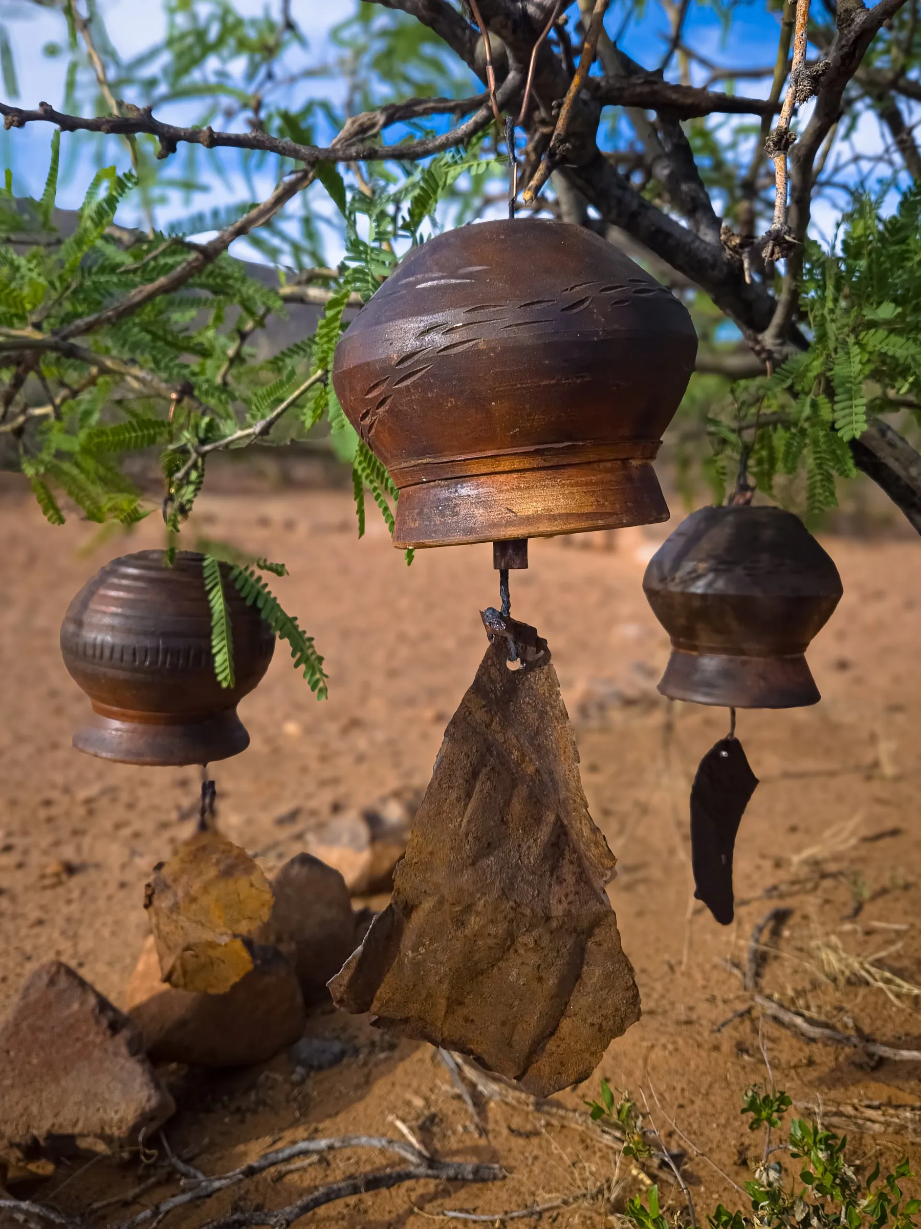 Clay bells hanging from a tree branch over red earth