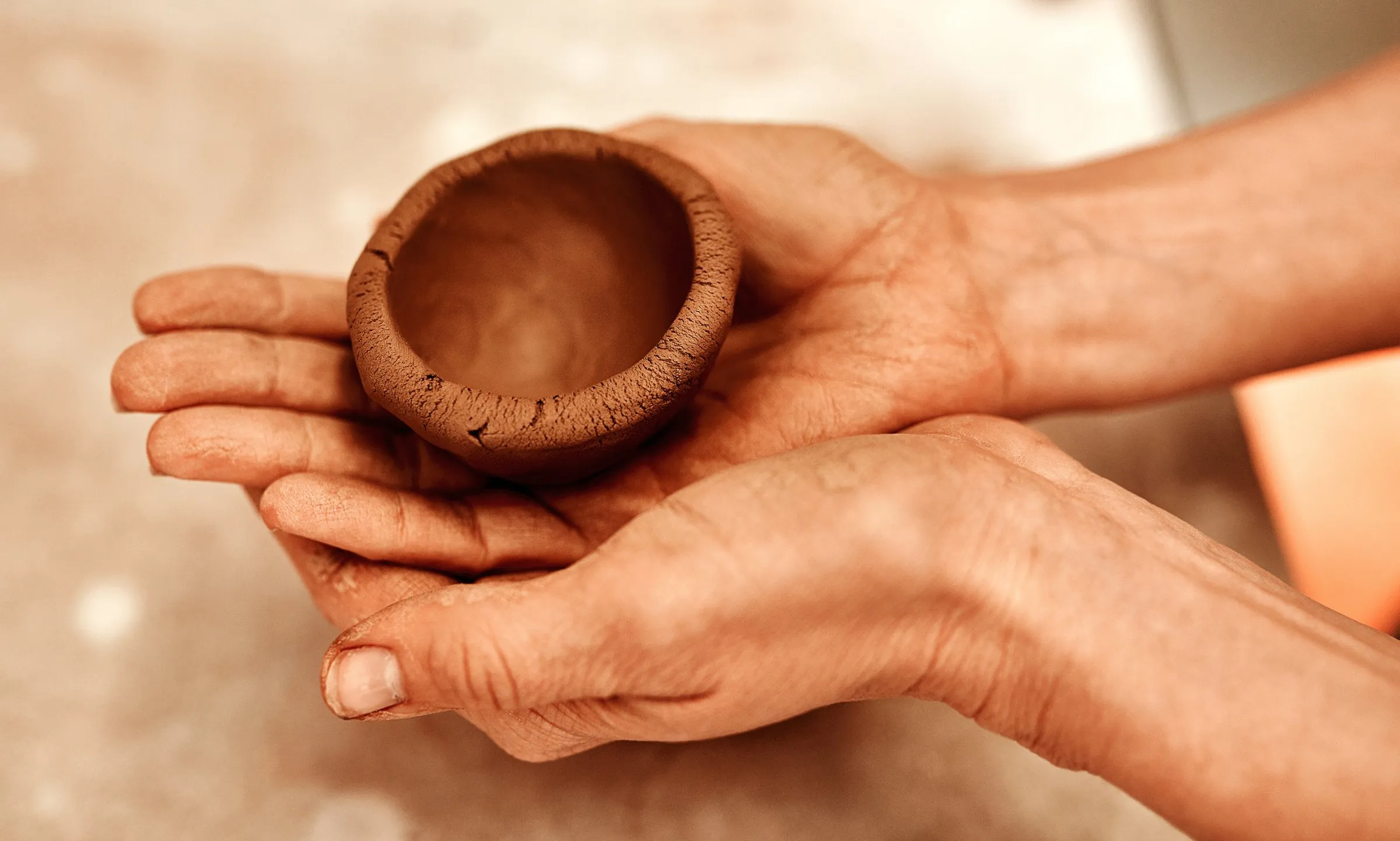 Two open hands holding a small handmade clay bowl