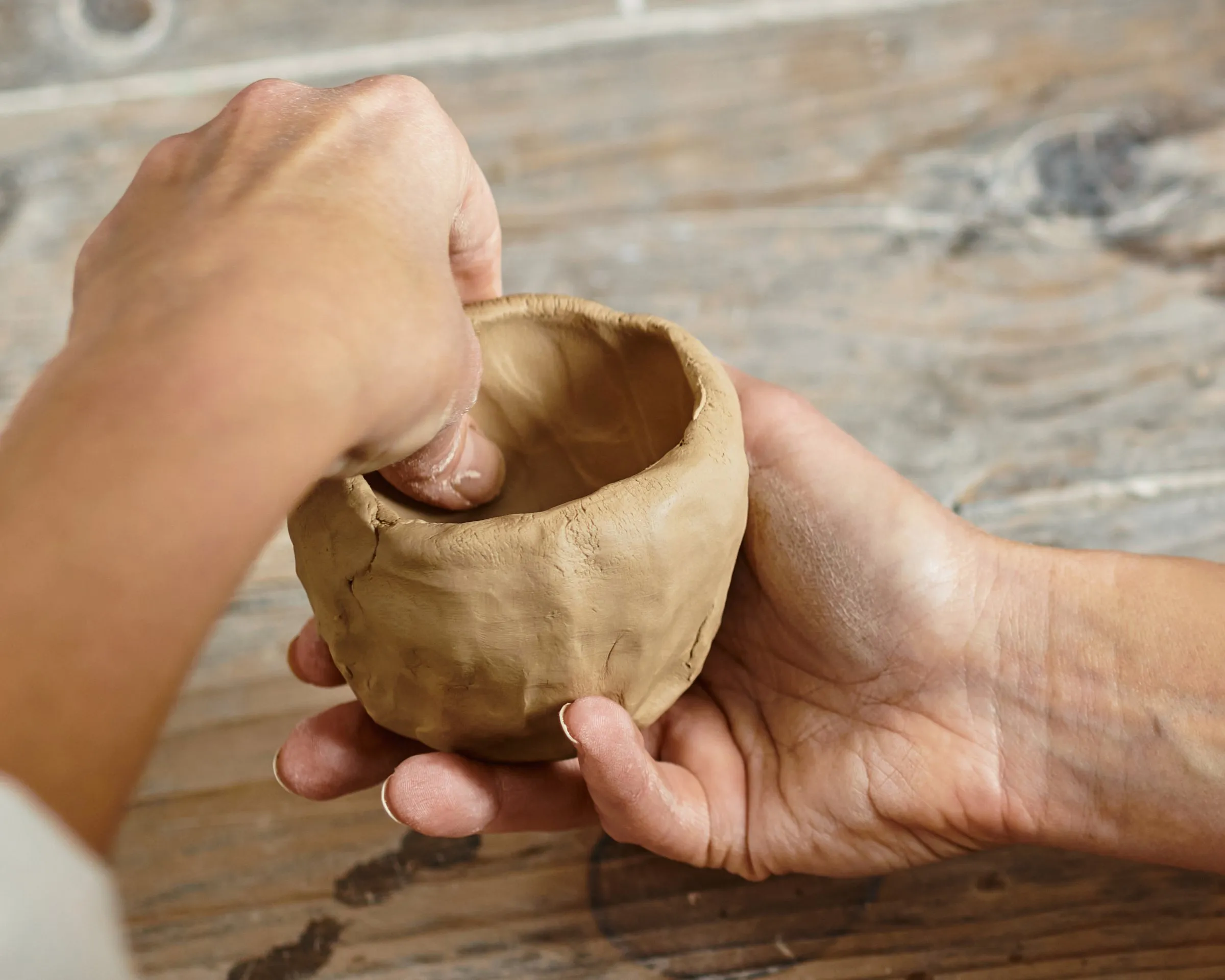 A hand pinching a small clay pot into shape
