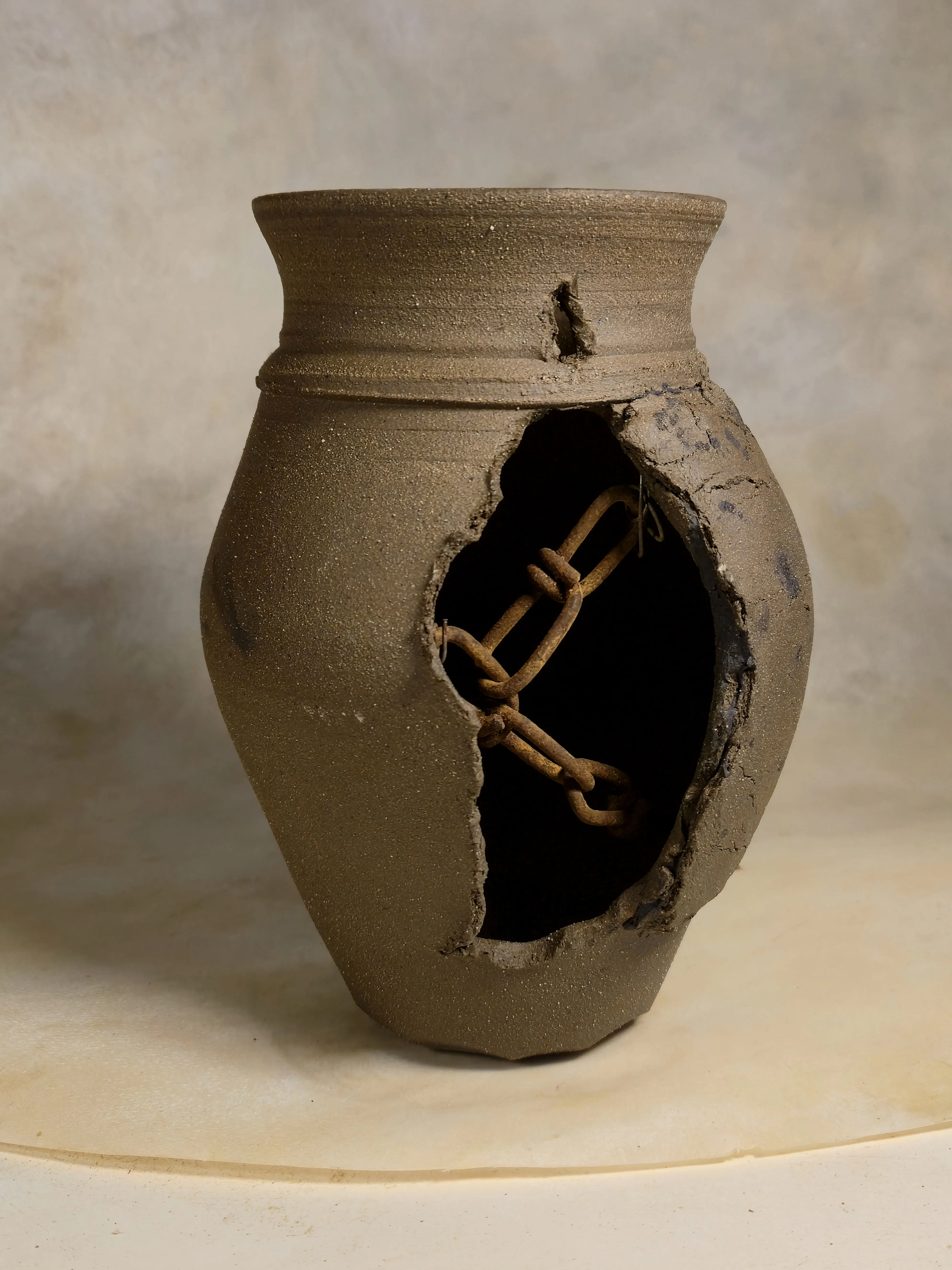 A sand-colored vessel with a ruptured side revealing a length of rusted chain stretched inside.